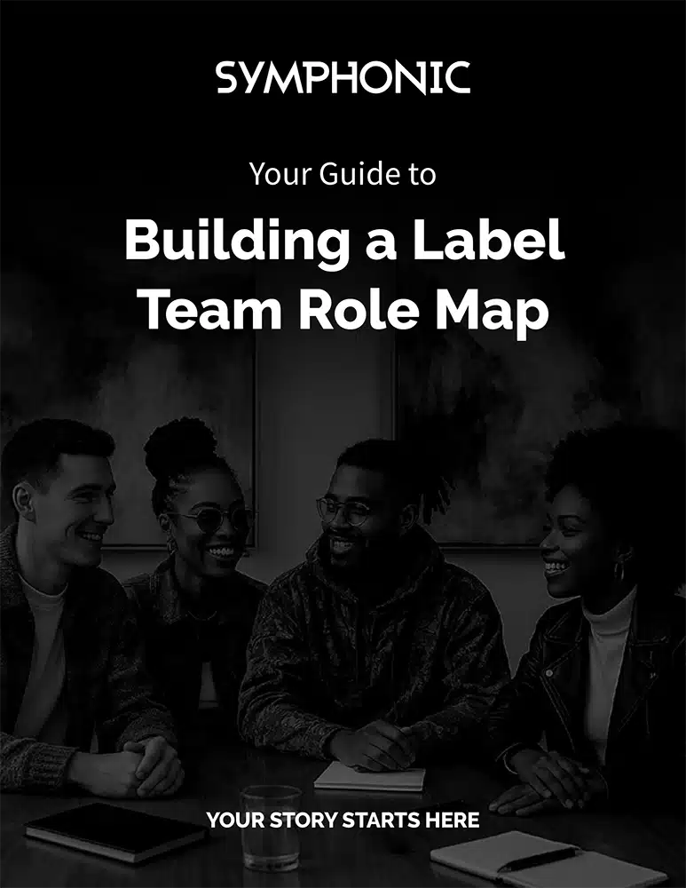 Four people sit and talk around a table with notebooks, under text that reads "Building a Label Team Role Map" by Symphonic—a valuable resource among music industry guides.